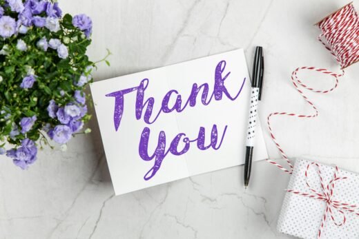 A stylish thank you card paired with purple flowers, a gift box, and pen on a marble surface.