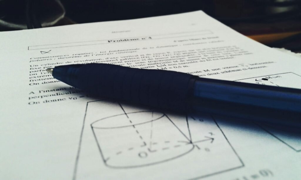 Close-up shot of a physics document with a blue pen on top, focused on equations.